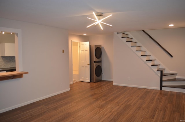 unfurnished living room with stairs, stacked washer / drying machine, baseboards, and wood finished floors