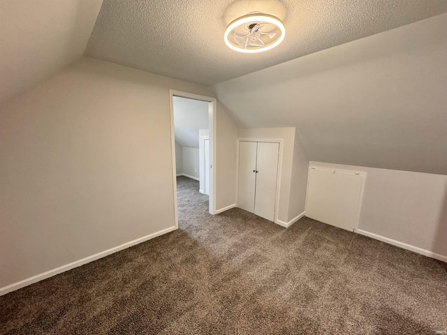 bonus room with lofted ceiling, dark carpet, a textured ceiling, and baseboards