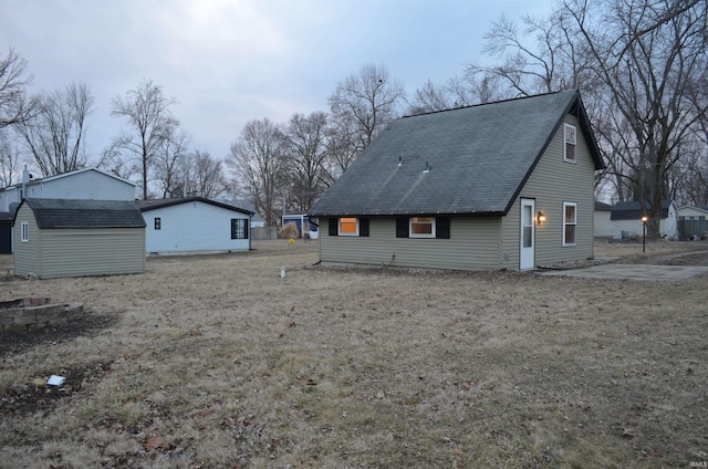 view of side of property with a storage shed, a shingled roof, and an outbuilding