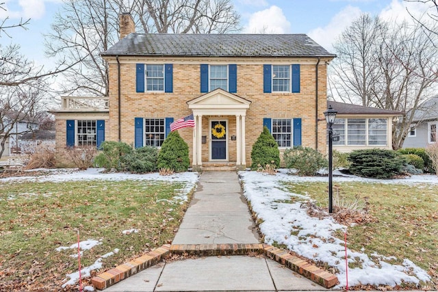 colonial home with brick siding, a chimney, and a lawn