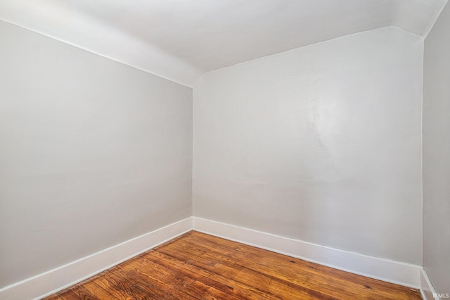 empty room featuring vaulted ceiling, baseboards, and wood finished floors