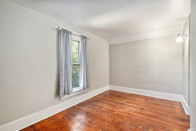 empty room featuring wood-type flooring, vaulted ceiling, and baseboards