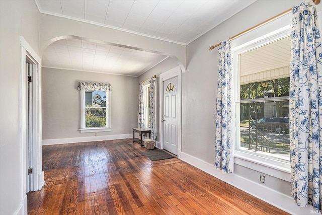 unfurnished room with arched walkways, crown molding, wood-type flooring, and baseboards