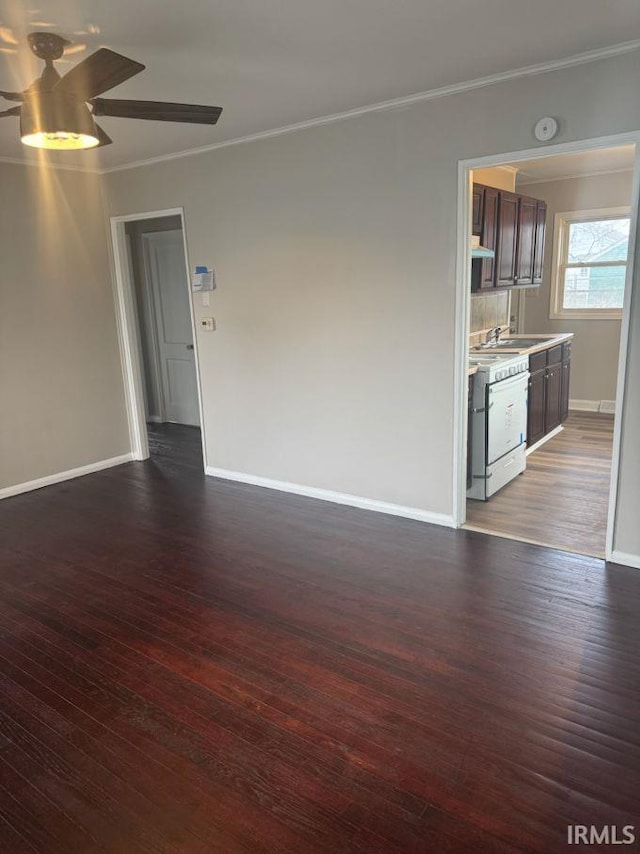 spare room with ceiling fan, a sink, baseboards, ornamental molding, and dark wood finished floors