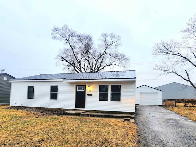 view of front facade featuring a garage, metal roof, aphalt driveway, an outdoor structure, and a front lawn