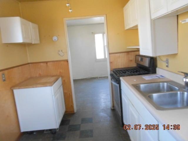 kitchen with a wainscoted wall, stainless steel range with gas cooktop, a sink, and wood walls