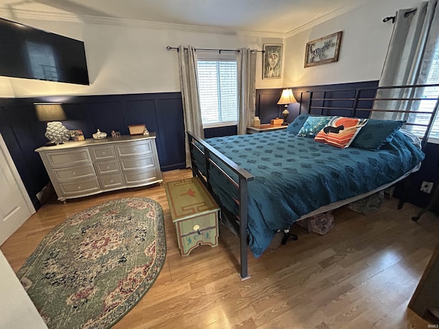 bedroom featuring a decorative wall, wainscoting, wood finished floors, and crown molding