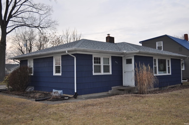 ranch-style home with a shingled roof, a chimney, and a front lawn