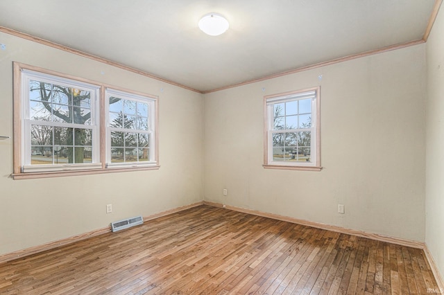 spare room with baseboards, light wood finished floors, visible vents, and crown molding