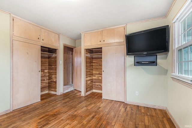 unfurnished bedroom featuring baseboards, hardwood / wood-style flooring, and multiple closets