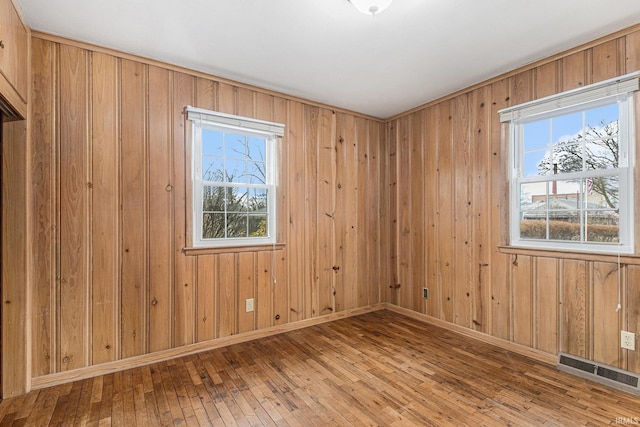 spare room featuring baseboards, wooden walls, visible vents, and hardwood / wood-style floors