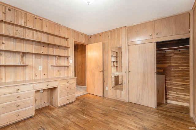 unfurnished bedroom with light wood-style flooring, wooden walls, a closet, and built in desk