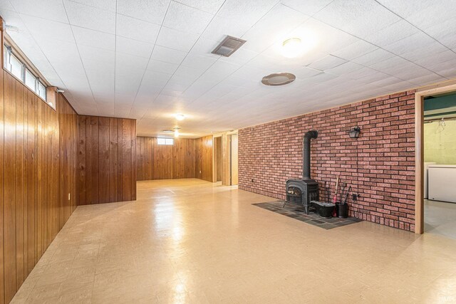 below grade area with a wood stove, visible vents, wooden walls, and tile patterned floors