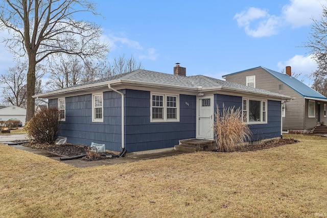 view of front of house featuring roof with shingles, a chimney, and a front lawn