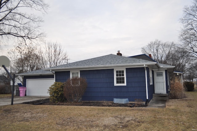 view of side of property with an attached garage, a shingled roof, concrete driveway, a lawn, and a chimney