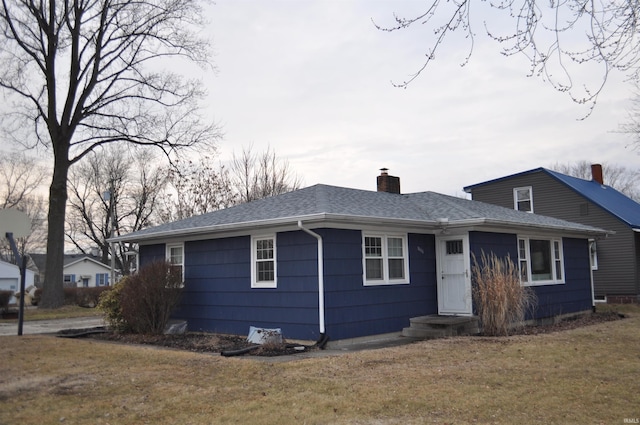 ranch-style house with a shingled roof, a chimney, and a front lawn