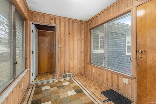 unfurnished room featuring brick floor, plenty of natural light, visible vents, and wooden walls