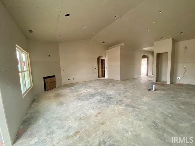 unfurnished living room with arched walkways and vaulted ceiling