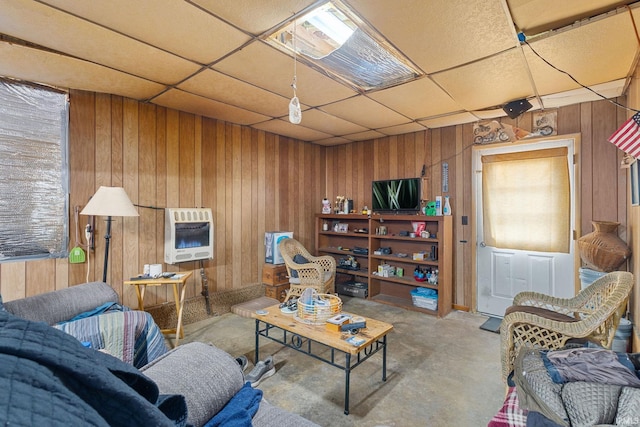 living area with a paneled ceiling, concrete floors, wooden walls, and heating unit