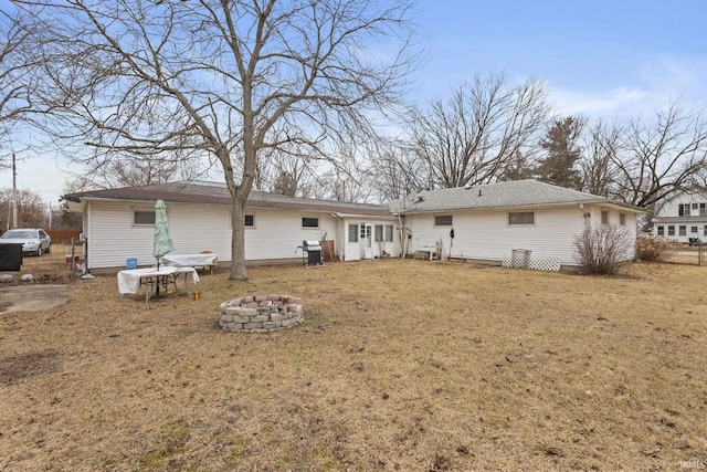 back of property with an outdoor fire pit and a lawn