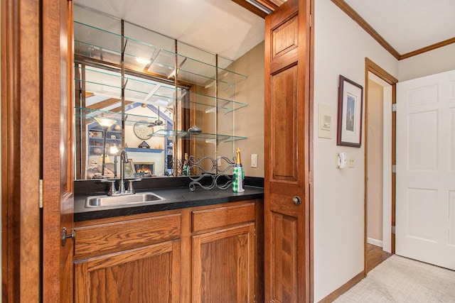 bar featuring indoor wet bar, crown molding, light colored carpet, a sink, and baseboards