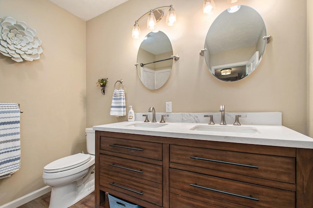 full bath with double vanity, wood finished floors, a sink, and toilet