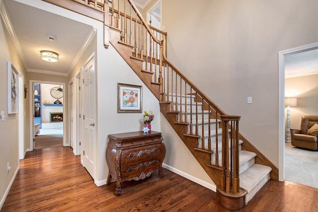 stairway featuring a lit fireplace, baseboards, crown molding, and wood finished floors