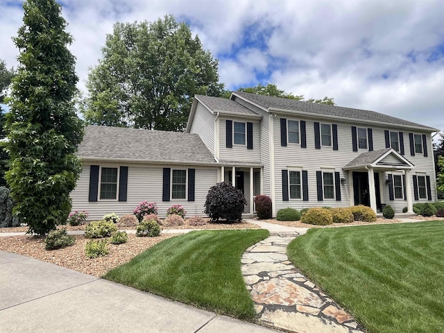 colonial inspired home with a shingled roof and a front yard