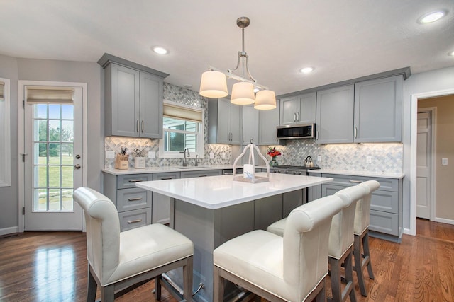 kitchen featuring a kitchen island, stainless steel microwave, dark wood-style flooring, gray cabinets, and light countertops