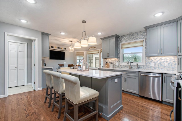 kitchen with a sink, dark wood finished floors, stainless steel dishwasher, and gray cabinetry