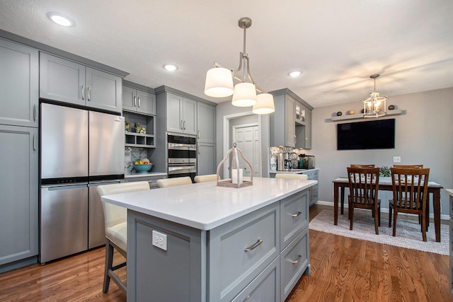 kitchen with a center island, stainless steel appliances, dark wood-style flooring, and gray cabinetry