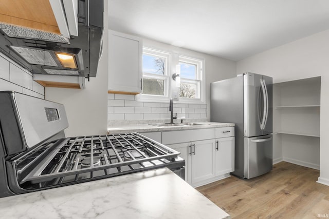 kitchen featuring a sink, light wood-style floors, white cabinets, appliances with stainless steel finishes, and backsplash