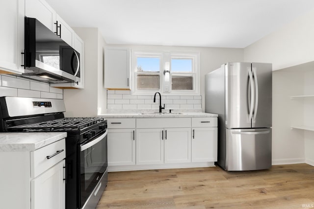 kitchen with tasteful backsplash, stainless steel appliances, light wood-type flooring, white cabinetry, and a sink