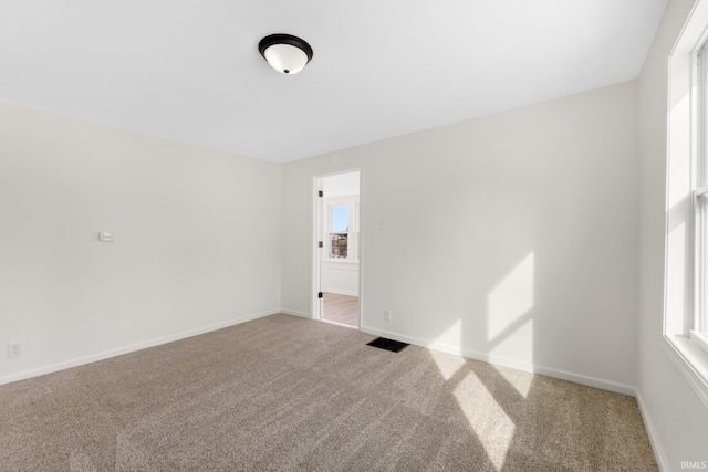 spare room featuring carpet floors, visible vents, and baseboards