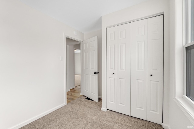 unfurnished bedroom with a closet, light carpet, and baseboards