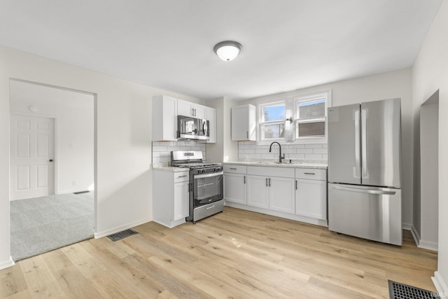 kitchen with a sink, visible vents, appliances with stainless steel finishes, light wood-type flooring, and decorative backsplash