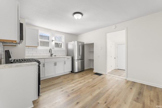 kitchen featuring light wood finished floors, stainless steel appliances, decorative backsplash, white cabinets, and a sink