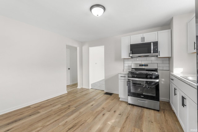 kitchen featuring baseboards, decorative backsplash, light wood-style flooring, appliances with stainless steel finishes, and light countertops