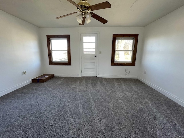 unfurnished room featuring plenty of natural light, dark carpet, and baseboards