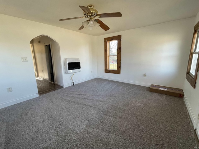 unfurnished living room featuring baseboards, arched walkways, a ceiling fan, heating unit, and carpet flooring