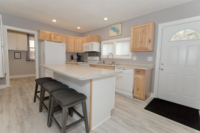 kitchen with light brown cabinets, white appliances, a sink, light countertops, and a kitchen bar