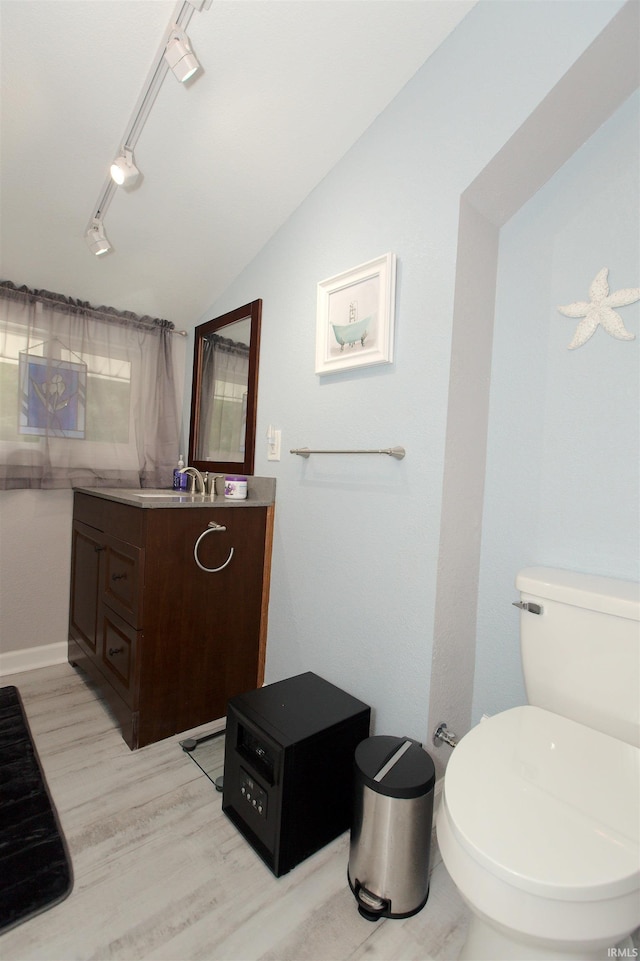 bathroom with lofted ceiling, toilet, wood finished floors, vanity, and track lighting