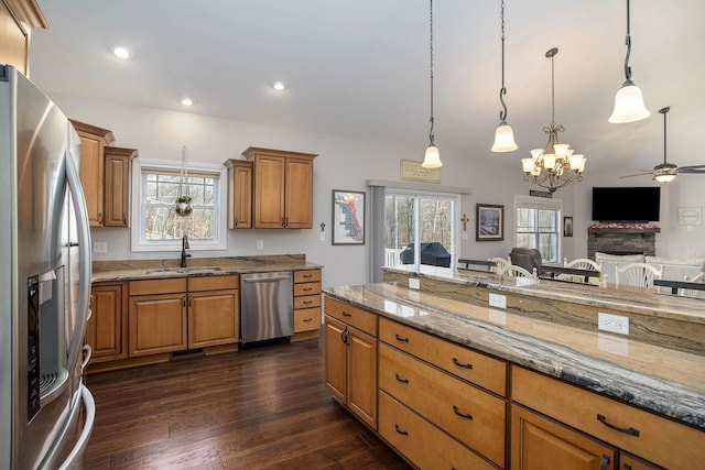 kitchen featuring light stone counters, dark wood finished floors, appliances with stainless steel finishes, brown cabinetry, and a sink