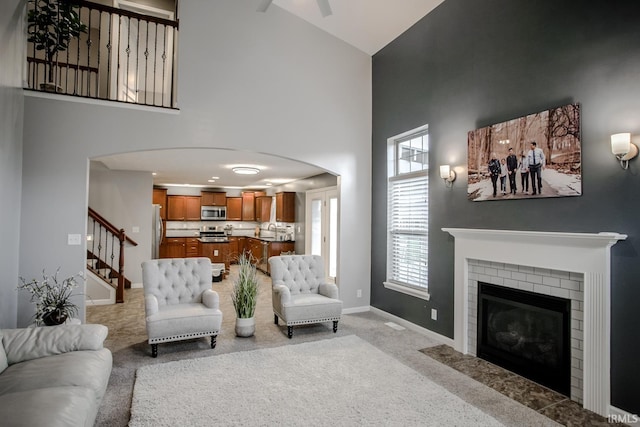 living area with light carpet, a high ceiling, baseboards, stairway, and a brick fireplace