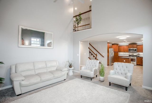 living room featuring baseboards, arched walkways, light colored carpet, a towering ceiling, and stairs