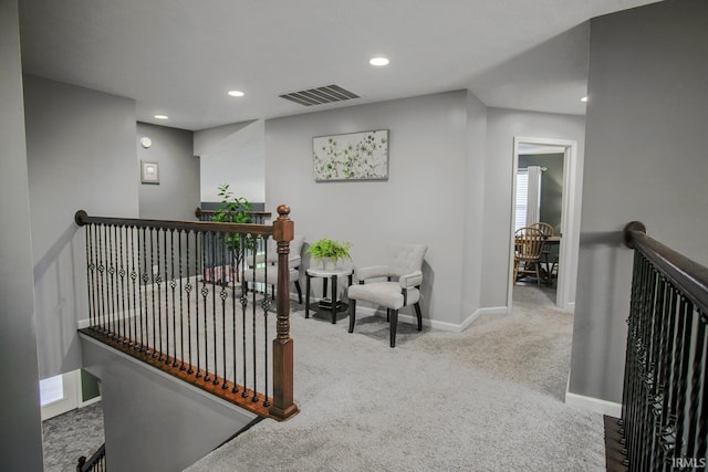 hallway featuring carpet floors, baseboards, visible vents, and an upstairs landing