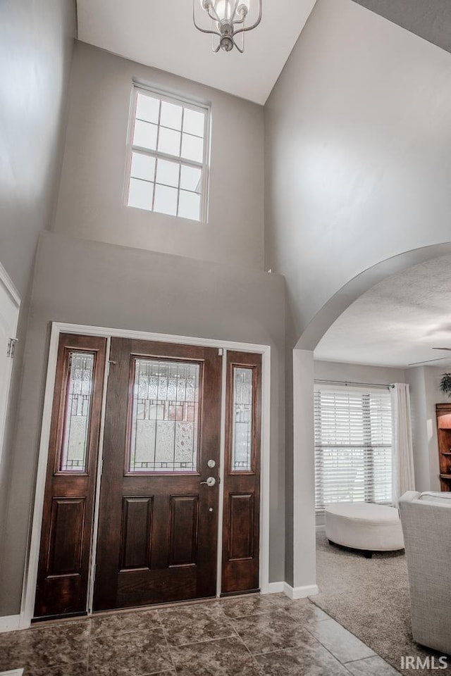 entryway featuring a towering ceiling, an inviting chandelier, baseboards, and arched walkways