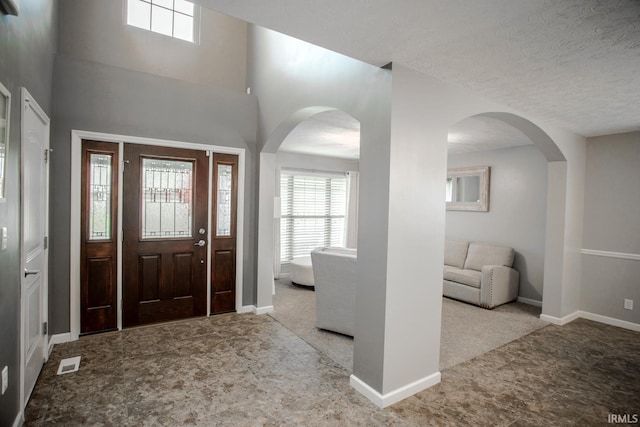 entrance foyer with arched walkways, a textured ceiling, visible vents, and baseboards