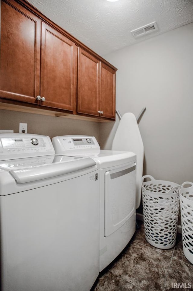 laundry room with washing machine and dryer, cabinet space, visible vents, and a textured ceiling