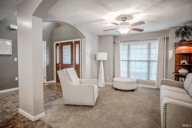 carpeted living area featuring arched walkways, a textured ceiling, a ceiling fan, and baseboards